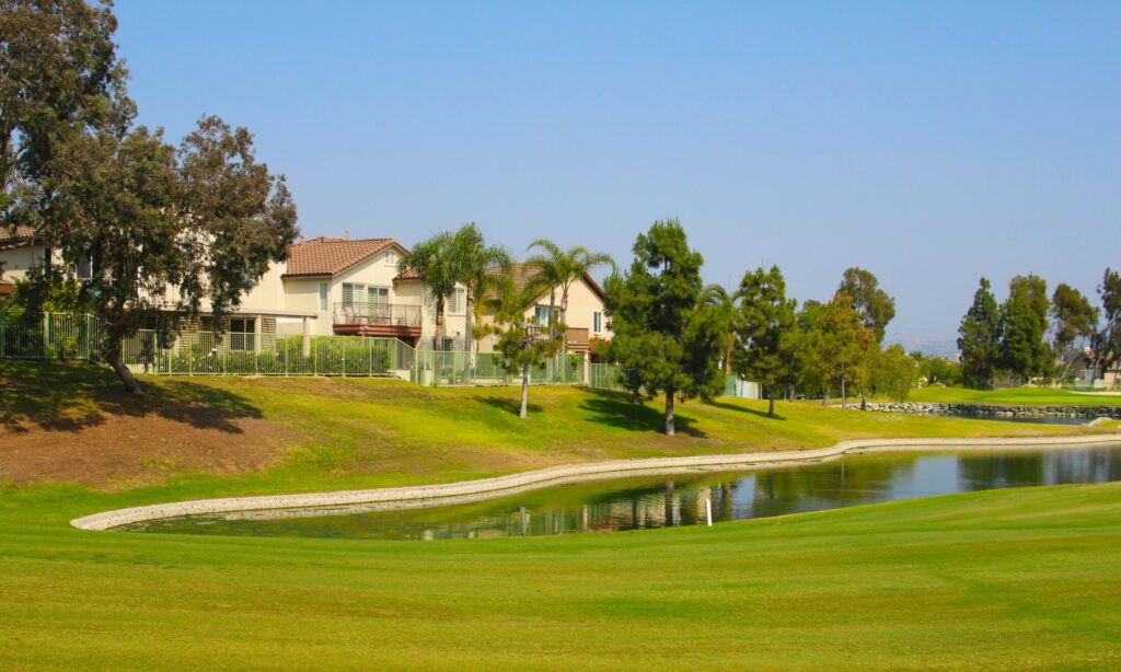 a man made lake in green grass golf course near houses and trees
